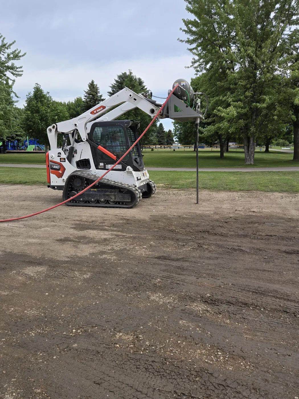 The track loader with the EarthBuster probe lowered into the ground on a job, red air hose running from the compressor