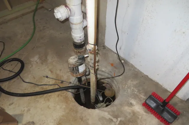 Before: an old sump pump and discharge pipe in a basement pit